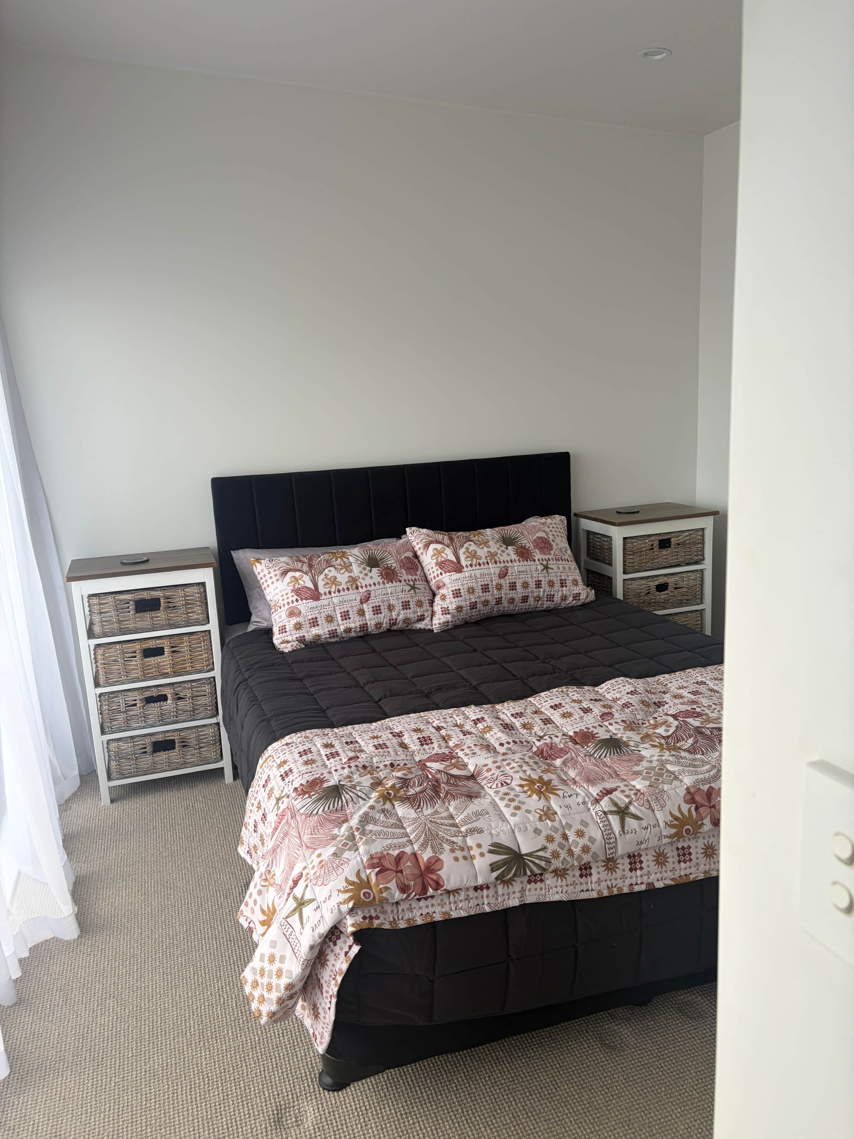 Una camera da letto con una testiera scura, una coperta con motivo floreale e due comodini con cesti in vimini.
