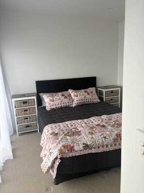 A bedroom with a dark headboard, a floral-patterned bedspread, and two nightstands with wicker baskets. - Sandy Soul Beach Apartment (Whitianga)