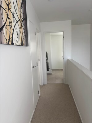 A hallway with a textured carpet, white walls, and a door leading to another room. - Sandy Soul Beach Apartment (Whitianga)