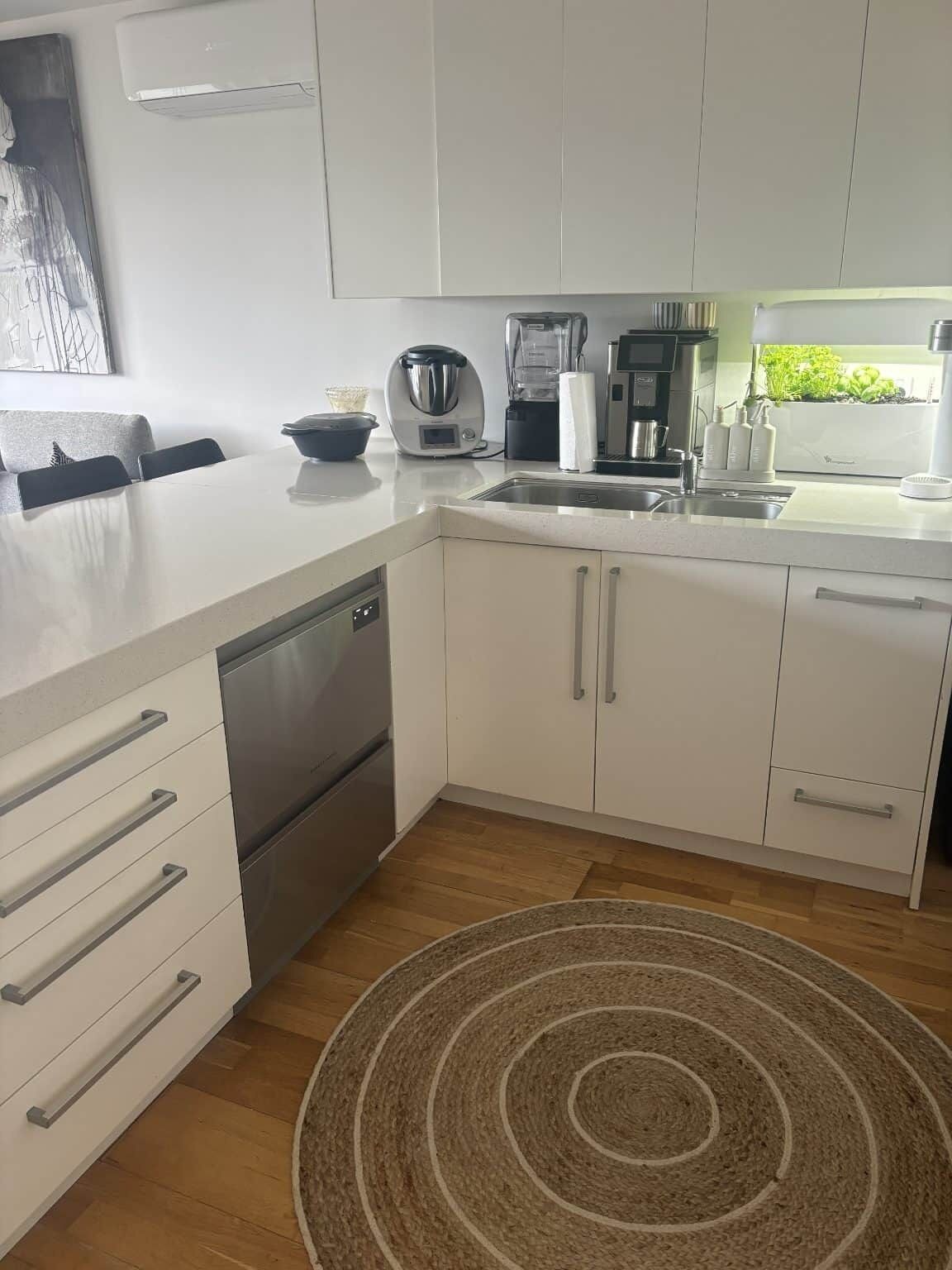 Una cocina moderna con armarios blancos, lavavajillas y cafetera.