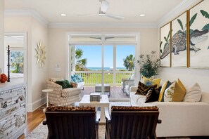 A spacious living room with a view of the ocean, a ceiling fan, and a dining area with a table and chairs. - Oceanfront 5BR home with private pool, hot tub, boardwalk & beach access. (Isle Of Palms)