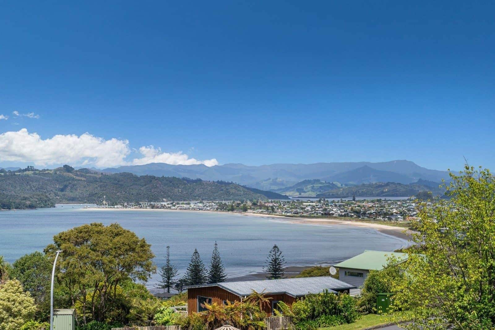 A coastal landscape with a clear view of the sea, a beach, and a town in the distance.