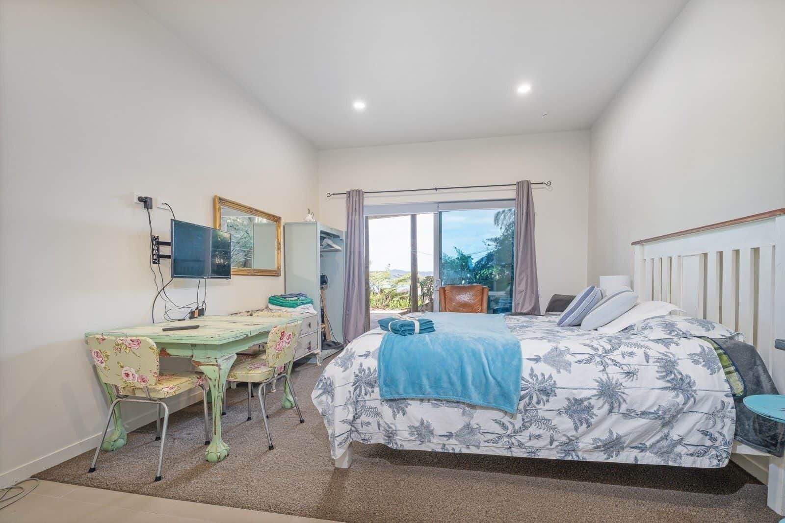 A bedroom with a bed, a desk, a chair, a mirror, and a window with curtains.