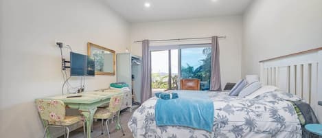 A bedroom with a bed, a desk, a chair, a mirror, and a window with curtains.