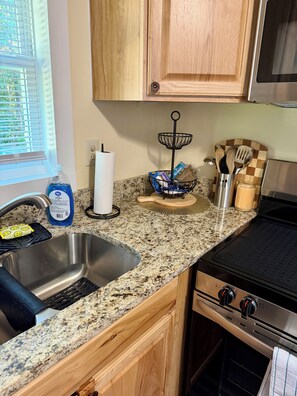 A kitchen with a granite countertop, stainless steel sink, wooden cabinets, a black stove, and a window with blinds. - Skip's Riverside Hideaway
Cozy 1-bedroom house in serene Conway, SC (Conway)