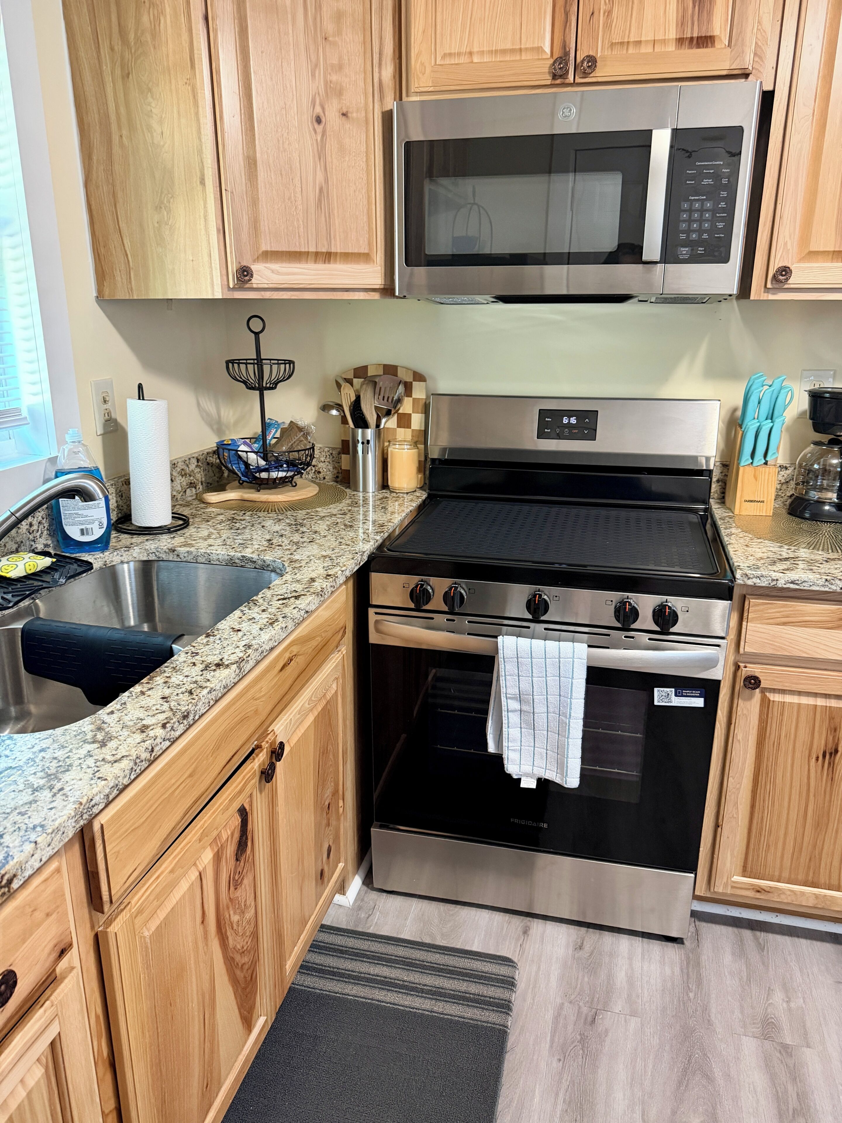 A kitchen with wooden cabinets, a stainless steel microwave, a stove, and a sink.