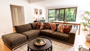 A modern living room with a sectional sofa, a round coffee table, and a dining area with a wooden table and chairs. - Stoke and Steam - the ultimate pad for adventurers (Bright)