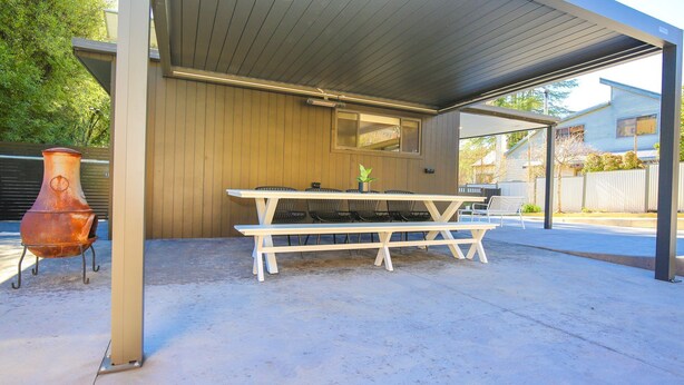 Eine Terrasse im Freien mit gedecktem Tisch und Stühlen, einem Grill und einem Blumentopf.