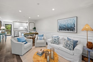 A spacious living room with a white sofa set, striped armchairs, and a coffee table with decorative items. - The Tidal Cottage - Beach Access + Pools (Hilton Head Island)