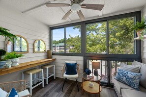 Ein Zimmer mit Deckenventilator, großen Fenstern, einer Bank, einem Sessel, einem kleinen Tisch und einem Sofa.
