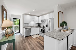 A modern kitchen with white cabinets, stainless steel appliances, and a granite countertop. - The Tidal Cottage - Beach Access + Pools (Hilton Head Island)