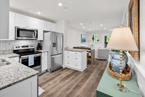 A modern kitchen with white cabinetry, stainless steel appliances, and a granite countertop. - The Tidal Cottage - Beach Access + Pools (Hilton Head Island)
