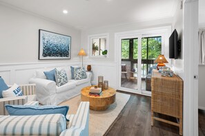 Ein modernes Wohnzimmer mit einem weißen Sofa, gestreiften Kissen, einem runden Couchtisch und einem großen Fenster mit Blick auf Grünflächen.