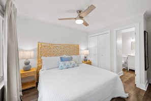 A bedroom with a bed, two bedside tables, a ceiling fan, a wooden headboard, and a white door. - The Tidal Cottage - Beach Access + Pools (Hilton Head Island)