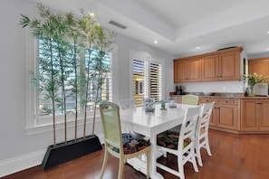 A modern kitchen with white cabinetry, a dining table with chairs, and large windows with bamboo plants. - Luxury Downtown Retreat | Steps to 5th Ave & Beach (Naples)