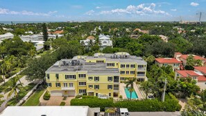 A multi-story building with a swimming pool, surrounded by greenery and other residential structures. - Luxury Downtown Retreat | Steps to 5th Ave & Beach (Naples)