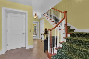 Un couloir avec une porte blanche, un escalier avec des rampes en bois et un canapé vert à motifs.