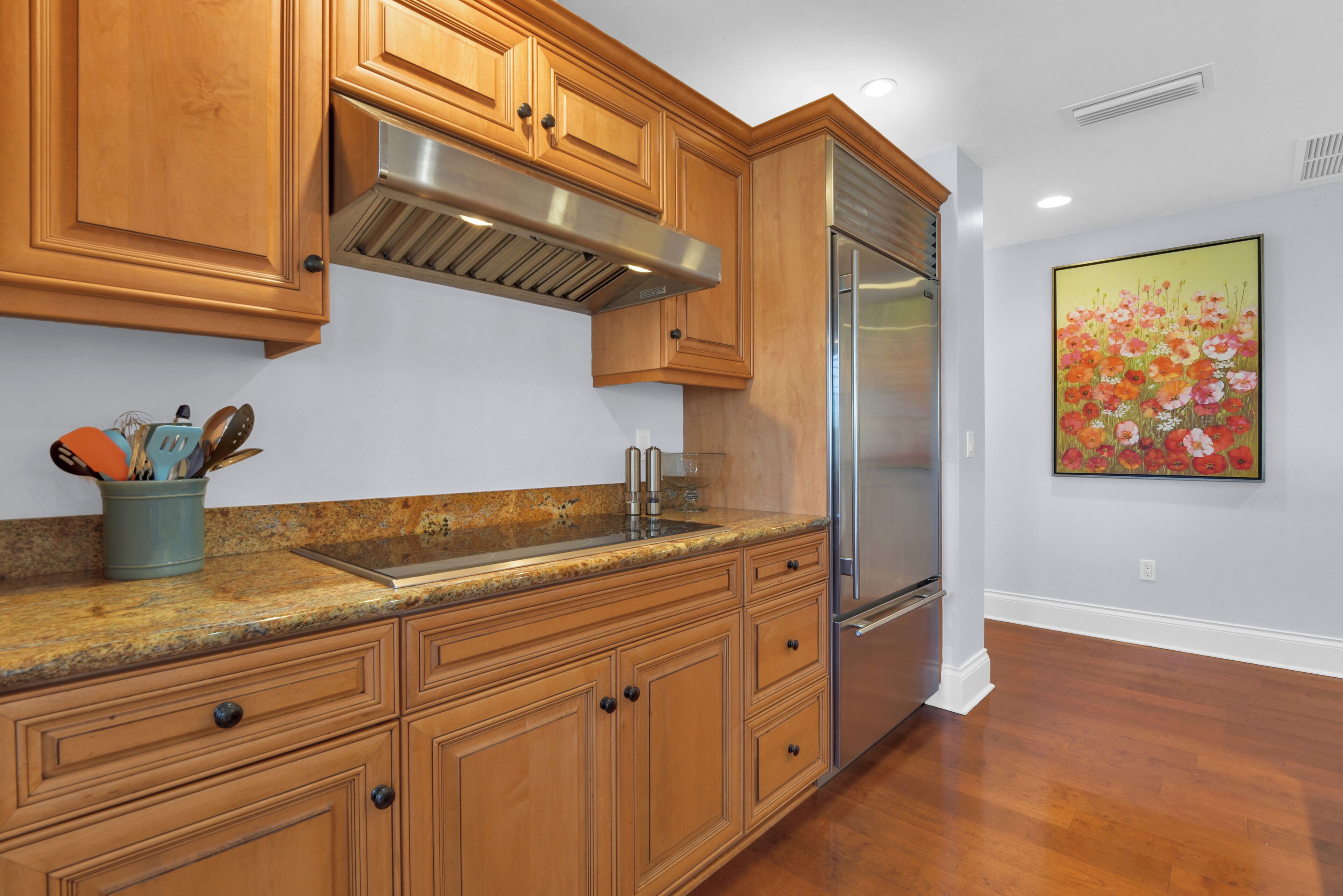 A kitchen with wooden cabinets, a stainless steel refrigerator, and a granite countertop.