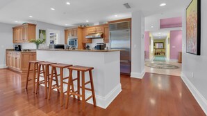 A modern kitchen with wooden cabinets, stainless steel appliances, and a central island with bar stools. - Luxury Downtown Retreat | Steps to 5th Ave & Beach (Naples)