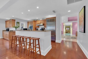 A modern kitchen with wooden cabinets, stainless steel appliances, and a central island with bar stools. - Luxury Downtown Retreat | Steps to 5th Ave & Beach (Naples)