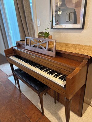 Un piano de cola en una habitación con piso de baldosas, un cuadro enmarcado en la pared y una planta sobre el piano.