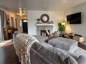 A modern living room with a sectional sofa, a fireplace, a mounted TV, and a dining area with a piano. - Lovely 3-bedroom house near large dog park (Lodi)