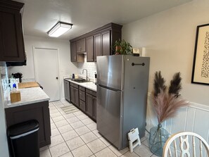 Una cocina con refrigerador de acero inoxidable, armarios de madera oscura, encimera blanca y suelo de baldosas.
