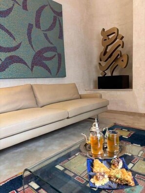 A living room with a sofa, a glass coffee table with drinks and snacks, and a wall art piece. - The Blue Room at Riad Timija: En-suite, Breakfast & Rooftop in the Medina (Marrakesh)
