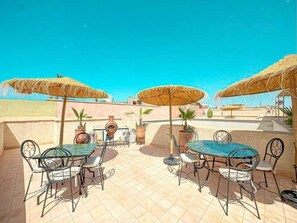 An outdoor patio with two round tables, metal chairs, and thatched umbrellas. - The Blue Room at Riad Timija: En-suite, Breakfast & Rooftop in the Medina (Marrakesh)