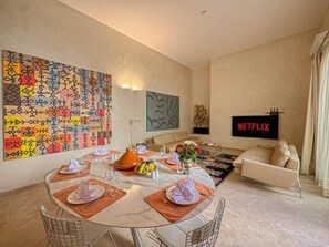 A dining area with a round table set for four, a sofa, and a flat-screen TV displaying 'NETFLIX'. - The Double Room at Riad Timija: En-suite, Breakfast & Rooftop in the Medina (Marrakesh)