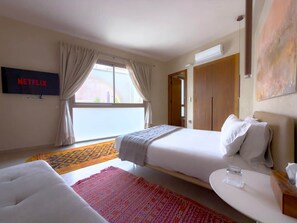 A hotel room with a bed, a sofa, a TV, and a window with curtains. - The White Room at Riad Timija: En-suite, Breakfast & Rooftop in the Medina (Marrakesh)