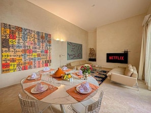 A dining area with a round table set for four, a sofa, and a flat-screen TV displaying 'NETFLIX'. - The Red Room at Riad Timija: En-suite, Breakfast & Rooftop in the Medina (Marrakesh)