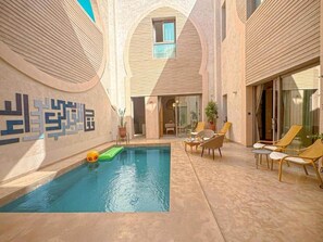 A swimming pool with lounge chairs and a glass door entrance. - The Red Room at Riad Timija: En-suite, Breakfast & Rooftop in the Medina (Marrakesh)