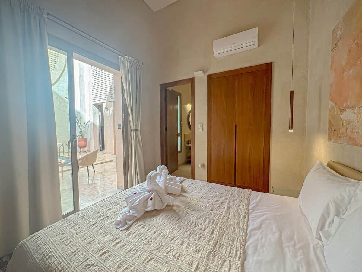 Une chambre d’hôtel comprenant un lit, une armoire en bois, une porte-fenêtre coulissante donnant sur un balcon et un appareil de climatisation fixé au mur.