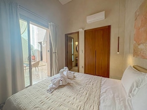 A hotel room with a bed, a wooden wardrobe, a sliding glass door leading to a balcony, and an air conditioning unit on the wall. - The Green Room at Riad Timija: En-suite, Breakfast & Rooftop in the Medina (Marrakesh)
