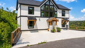 A modern two-story house with a large front porch, a garage, and a spacious driveway. - Gatlinburg Getaway with Hot Tub, Mountain Views, Theater, Game Room & Smoky Mountains (Gatlinburg)