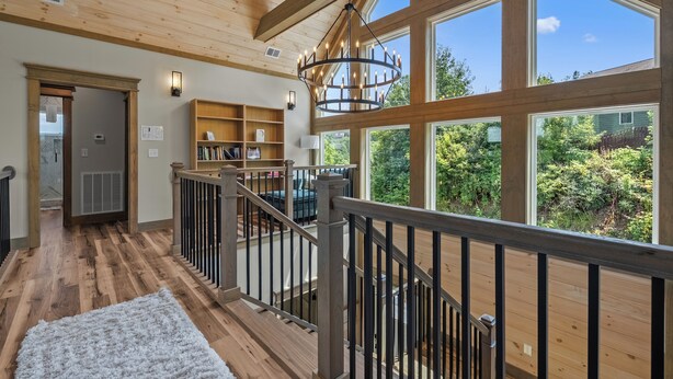 A spacious room with a wooden floor, a staircase with a railing, and large windows offering a view of greenery outside. - Gatlinburg Getaway with Hot Tub, Mountain Views, Theater, Game Room & Smoky Mountains (Gatlinburg)