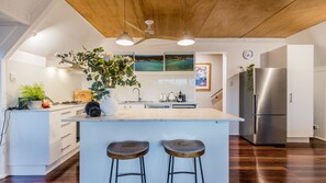 A modern kitchen with a central island, bar stools, a stainless steel refrigerator, and a ceiling fan. - Riverbank 1770  waterfront (Seventeen Seventy)