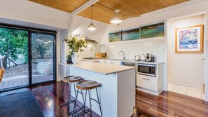 A modern kitchen with a large island, bar stools, and a view of the outdoors. - Riverbank 1770  waterfront (Seventeen Seventy)