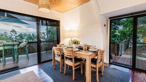 Un coin repas avec une table dressée pour quatre personnes, entourée de chaises, et offrant une vue sur la verdure à l’extérieur.