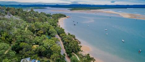 An aerial view of a coastal area with a beach, boats, and dense greenery.
