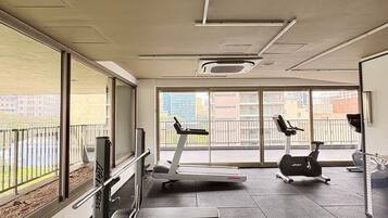 Uma academia com equipamentos de ginástica, janelas amplas e vista para a cidade.