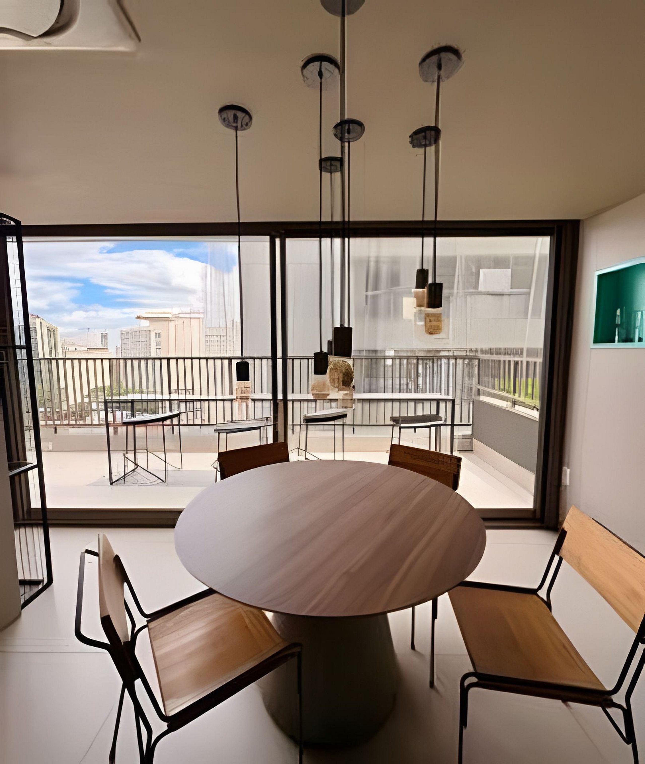 Uma área de jantar moderna com mesa redonda e cadeiras, grandes janelas com vista para a cidade e luminárias pendentes.