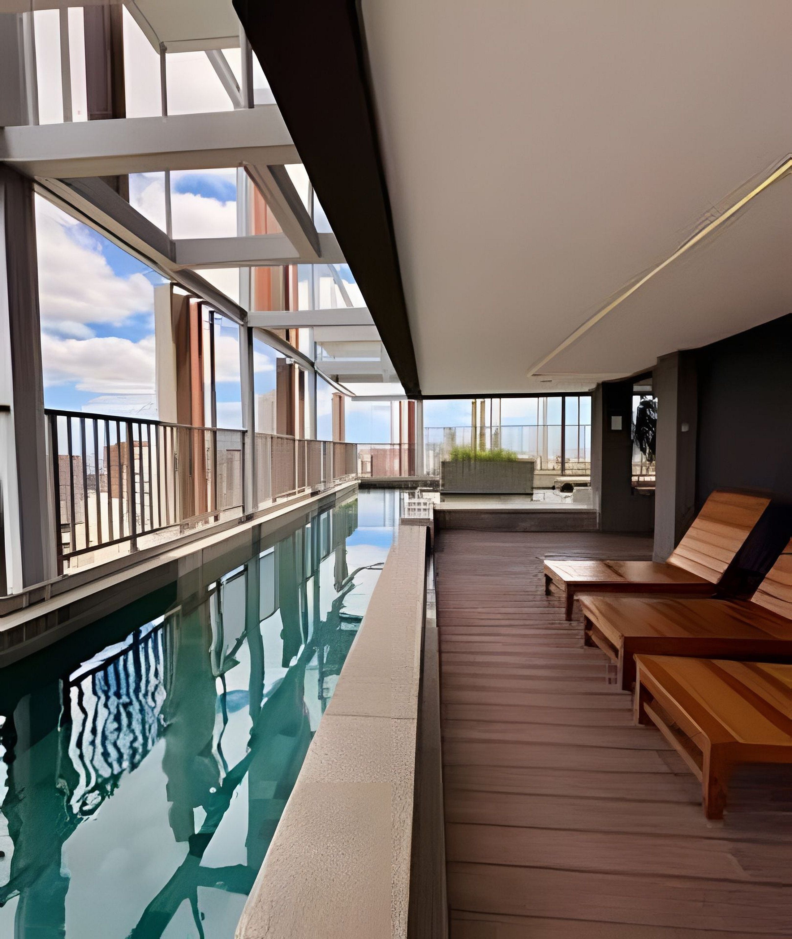 Uma área de piscina interior moderna, com paredes de vidro, deck de madeira e assentos de lounge.