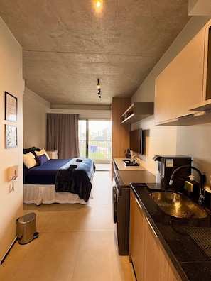 A compact hotel room with a bed, a kitchenette, a small bathroom, and a view of the city through the window. - On Melo Alves (São Paulo)