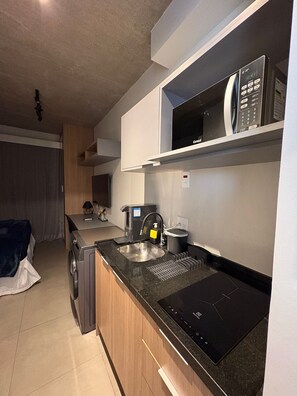 Una cocina compacta con microondas integrado, cafetera y lavamanos.