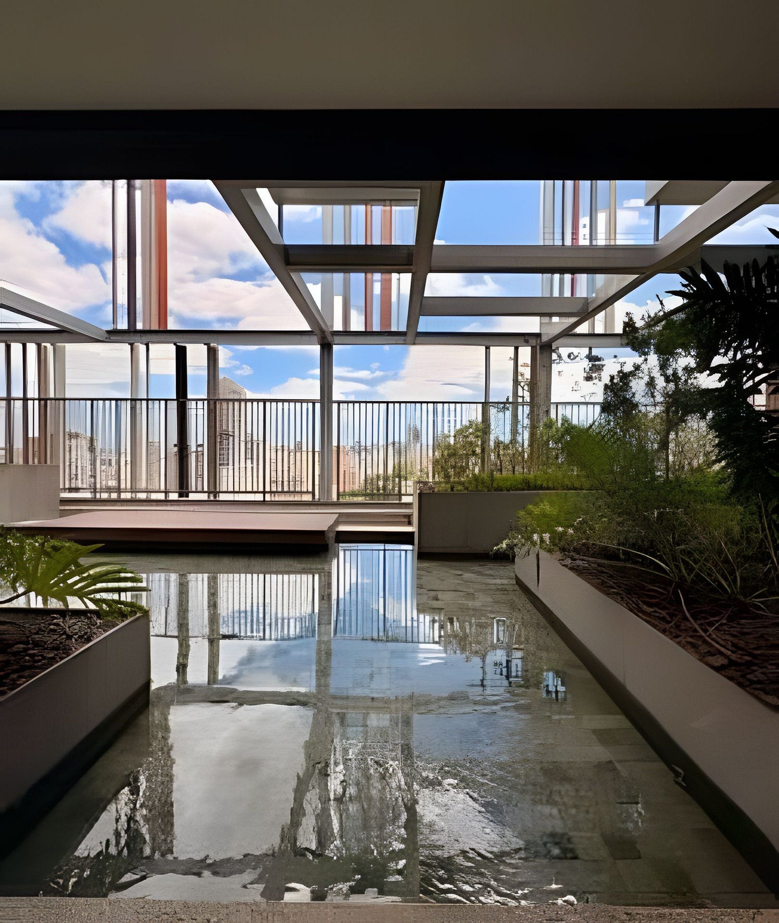 En moderne swimmingpool indendørs med glasvægge, omgivet af grønt og udsigt over bybilledet.