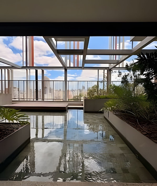 A modern indoor pool with clear glass walls, surrounded by greenery and a view of the cityscape. - On Melo Alves (São Paulo)