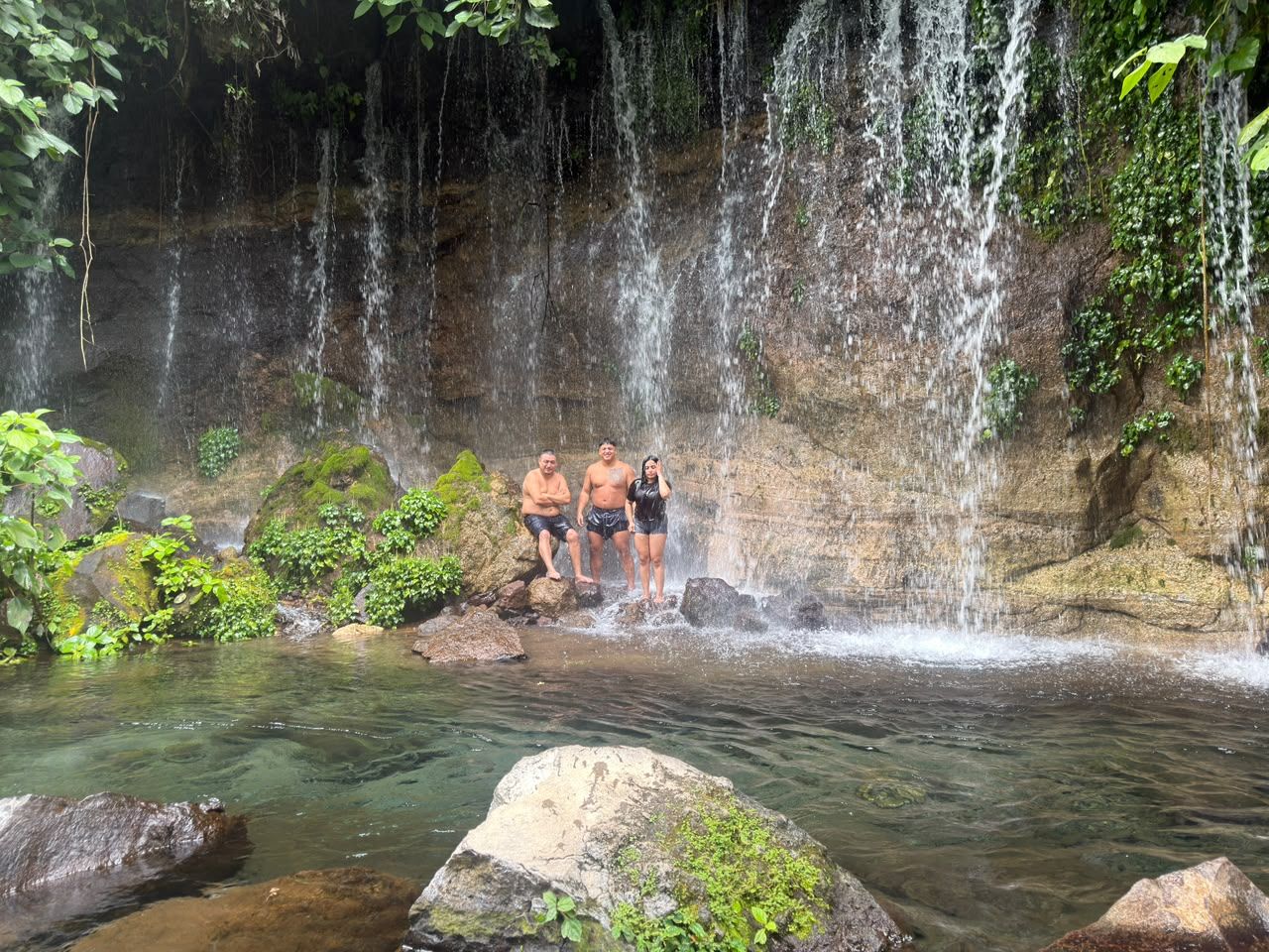 Ein natürlicher Wasserfall mit klarem Wasser, umgeben von Felsen und Grünpflanzen.