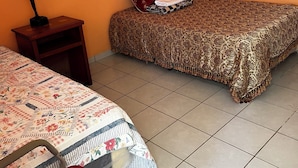 Une chambre avec deux lits, l’un recouvert d’une couvre-lit à motifs et l’autre d’une couvre-lit à fleurs. Il y a une table de chevet avec une lampe et une serviette pliée sur le lit.